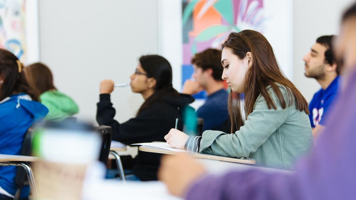 Female student writes at a desk in a classroom.